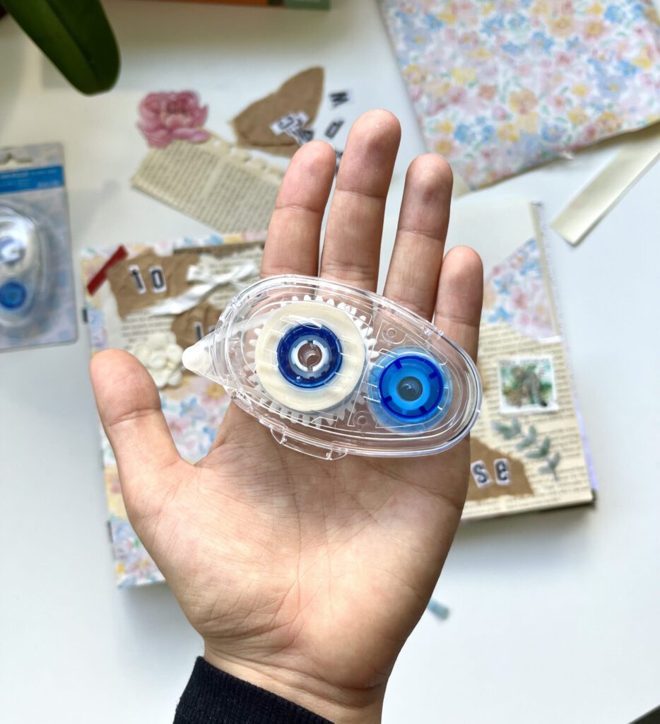 a hand holding a glue roller, in the background we see a bullet journal opened on an unfinished page