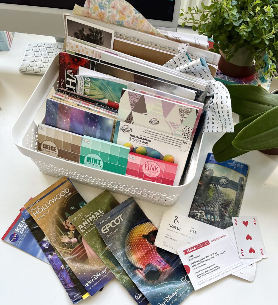 A box containing lots of decorative paper for journalling. You can see wrapping paper, magazines, note blocks and maps as well as tickets to shows and planes. In the background there is books and plants